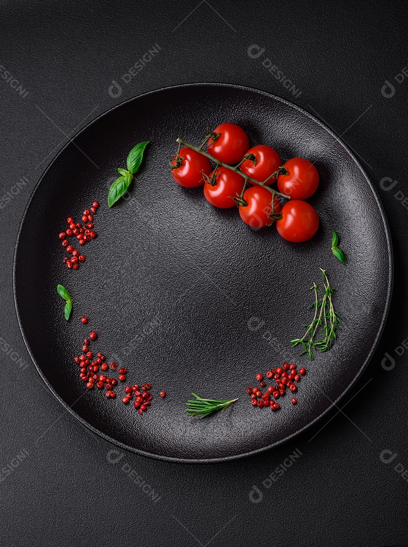 Ingredientes para cozinhar tomate cereja, sal, especiarias e ervas sobre um fundo escuro de concreto