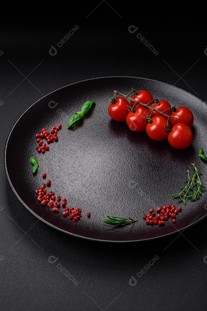 Ingredientes para cozinhar tomate cereja, sal, especiarias e ervas sobre um fundo escuro de concreto