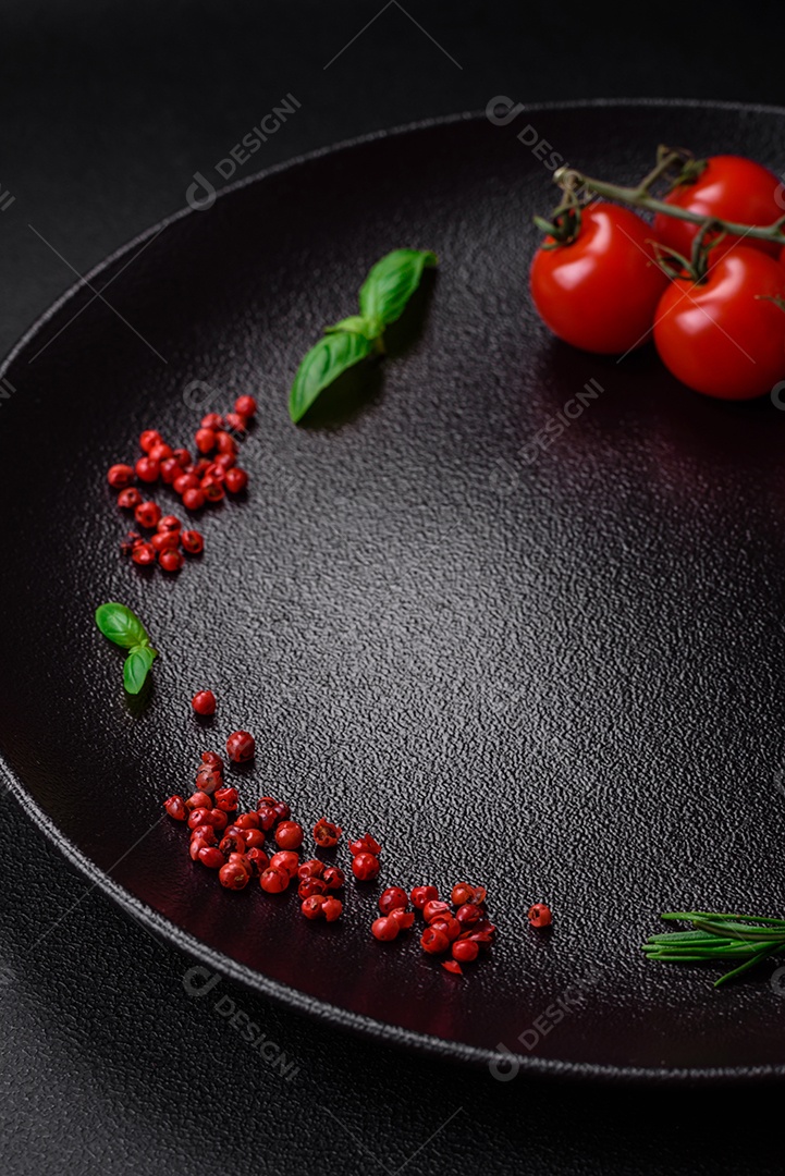 Ingredientes para cozinhar tomate cereja, sal, especiarias e ervas sobre um fundo escuro de concreto