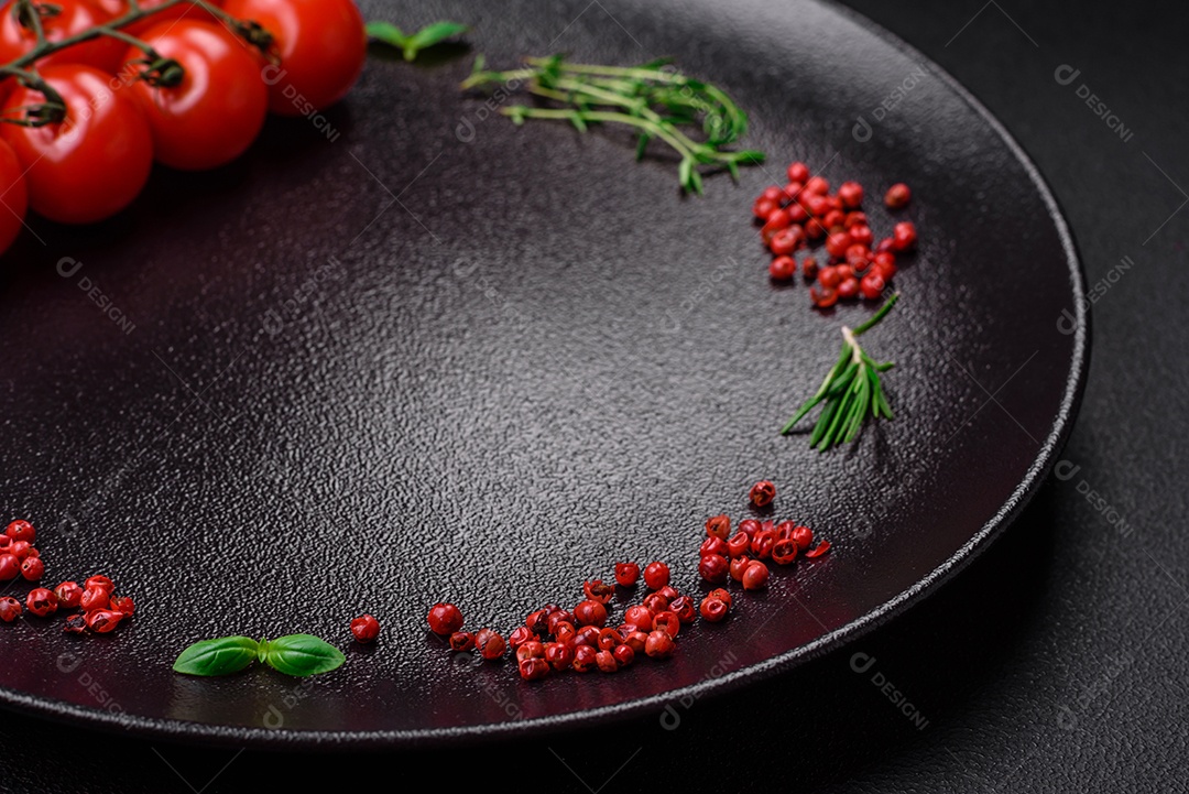 Ingredientes para cozinhar tomate cereja, sal, especiarias e ervas sobre um fundo escuro de concreto