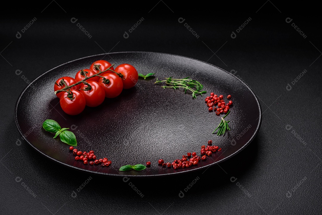 Ingredientes para cozinhar tomate cereja, sal, especiarias e ervas sobre um fundo escuro de concreto