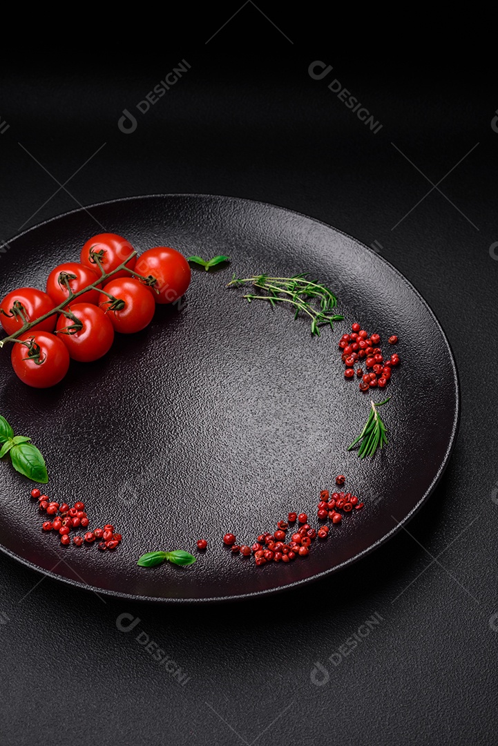 Ingredientes para cozinhar tomate cereja, sal, especiarias e ervas sobre um fundo escuro de concreto