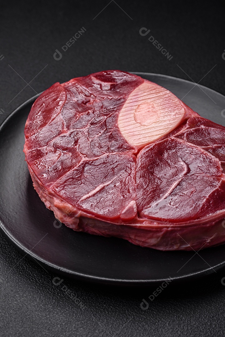 Bife de ossobuco de carne fresca com sal, especiarias e ervas em fundo de concreto texturizado