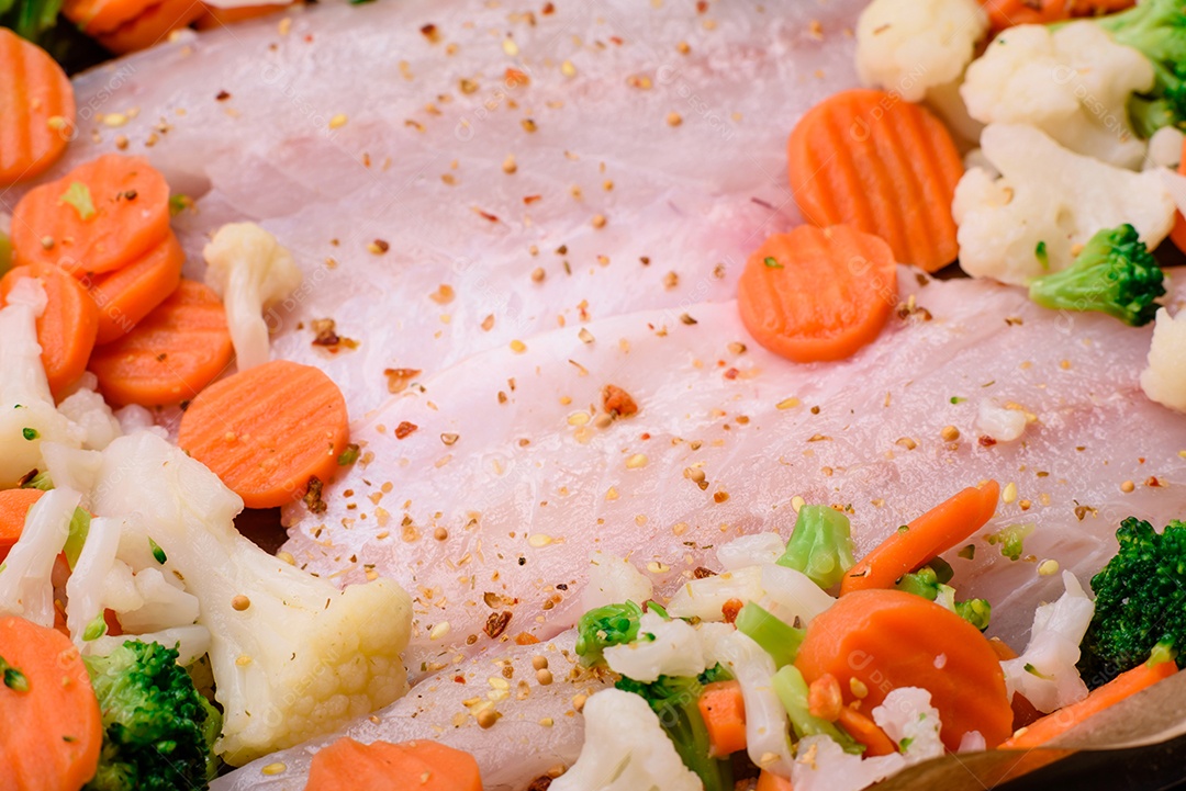 Filé de peixe robalo cru com sal, especiarias e legumes em uma assadeira sobre um fundo texturizado