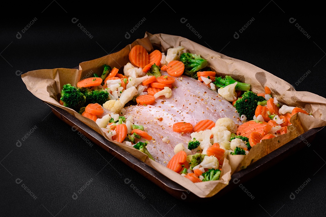 Filé de peixe robalo cru com sal, especiarias e legumes em uma assadeira sobre um fundo texturizado