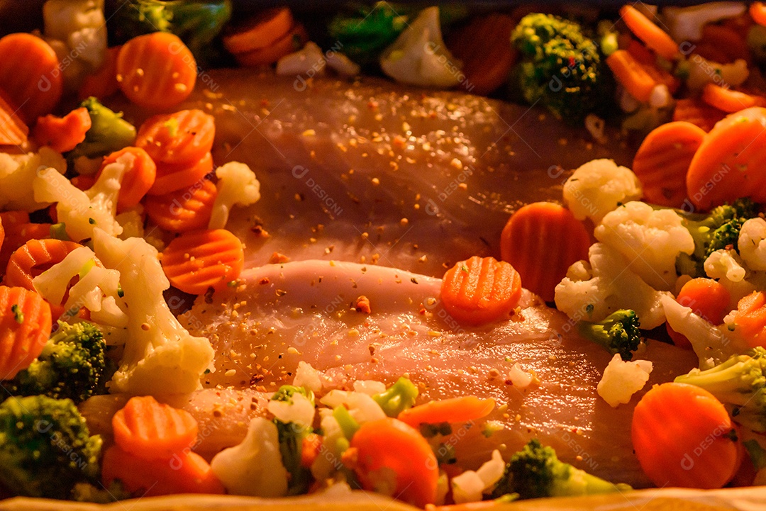 Filé de peixe robalo cru com sal, especiarias e legumes em uma assadeira sobre um fundo texturizado