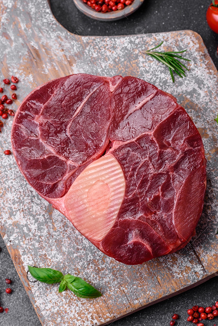 Bife de ossobuco de carne fresca com sal, especiarias e ervas em fundo de concreto texturizado