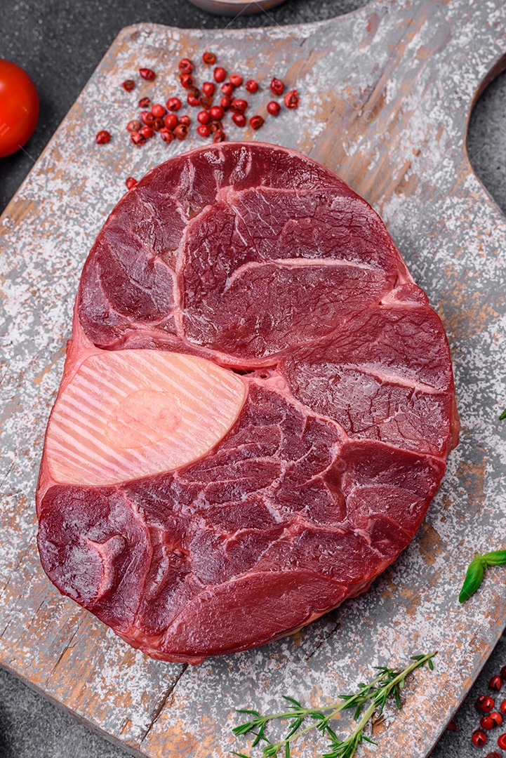 Bife de ossobuco de carne fresca com sal, especiarias e ervas em fundo de concreto texturizado