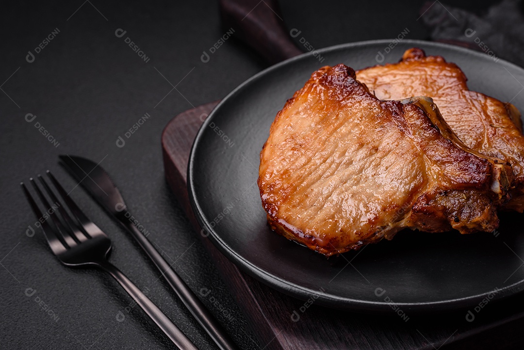 Delicioso suculento bife de porco ou de vaca com sal, especiarias e ervas sobre um fundo de concreto texturizado