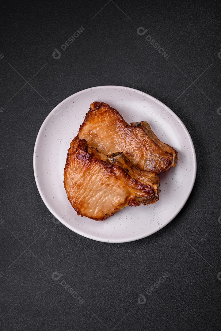 Delicioso suculento bife de porco ou de vaca com sal, especiarias e ervas sobre um fundo de concreto texturizado