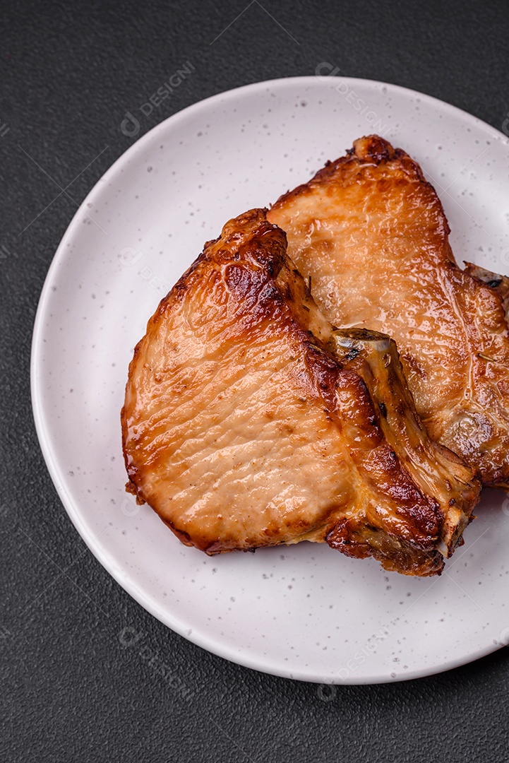 Delicioso suculento bife de porco ou de vaca com sal, especiarias e ervas sobre um fundo de concreto texturizado