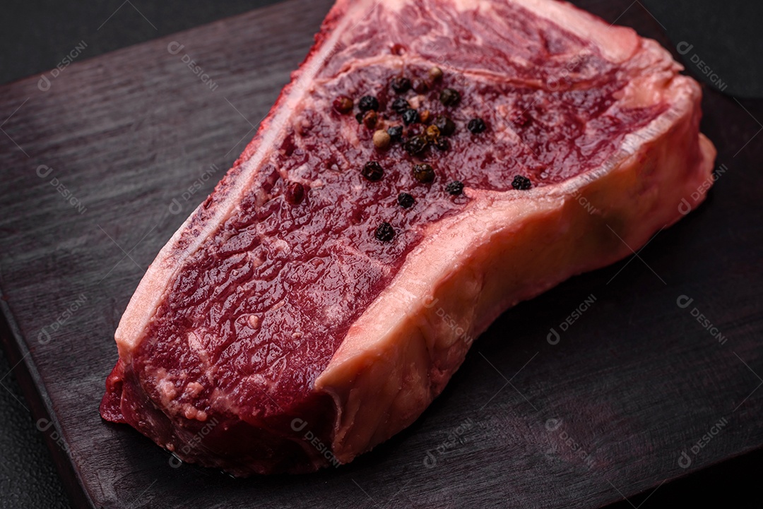 Bife fresco e suculento de Nova Iorque com sal, especiarias e ervas em fundo escuro de concreto