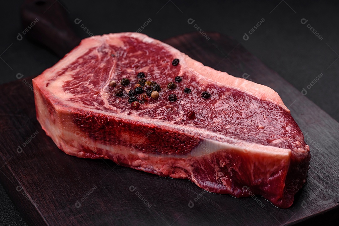 Bife fresco e suculento de Nova Iorque com sal, especiarias e ervas em fundo escuro de concreto