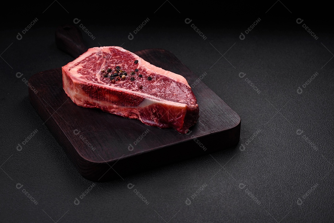 Bife fresco e suculento de Nova Iorque com sal, especiarias e ervas em fundo escuro de concreto