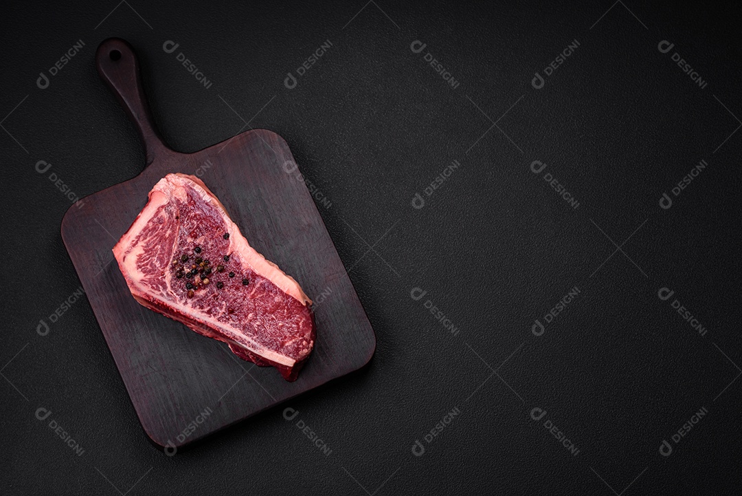 Bife fresco e suculento de Nova Iorque com sal, especiarias e ervas em fundo escuro de concreto