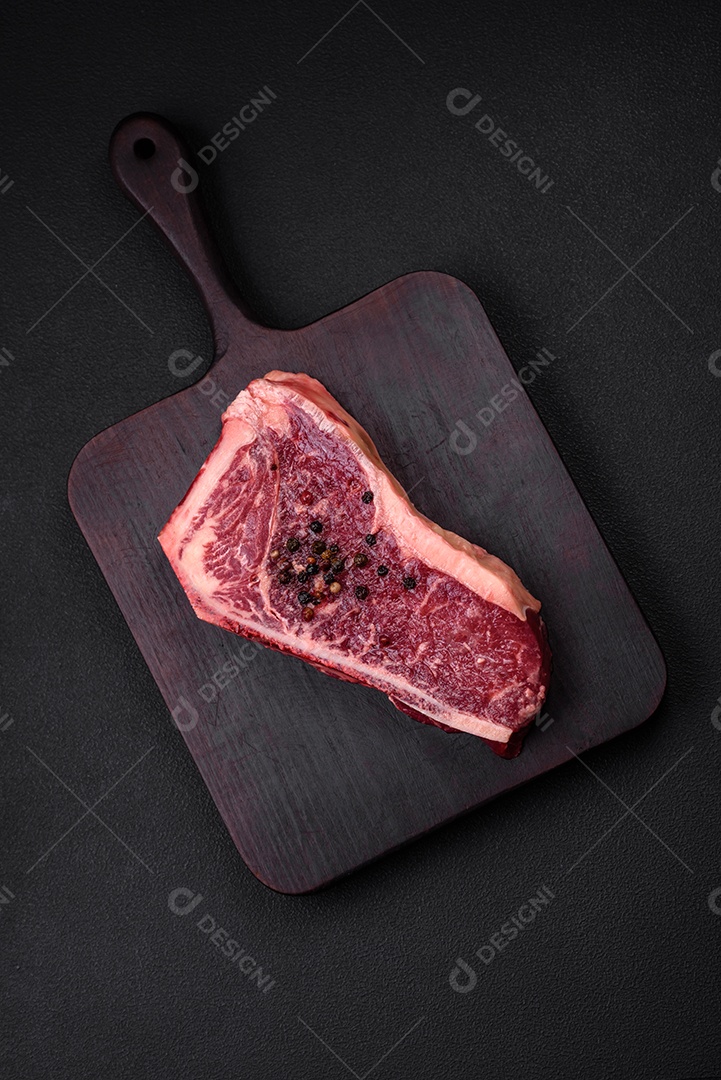 Bife fresco e suculento de Nova Iorque com sal, especiarias e ervas em fundo escuro de concreto