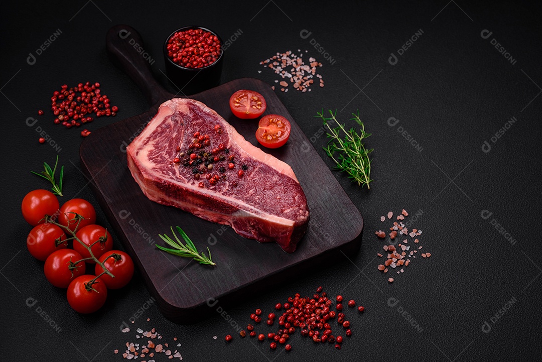 Bife fresco e suculento de Nova Iorque com sal, especiarias e ervas em fundo escuro de concreto