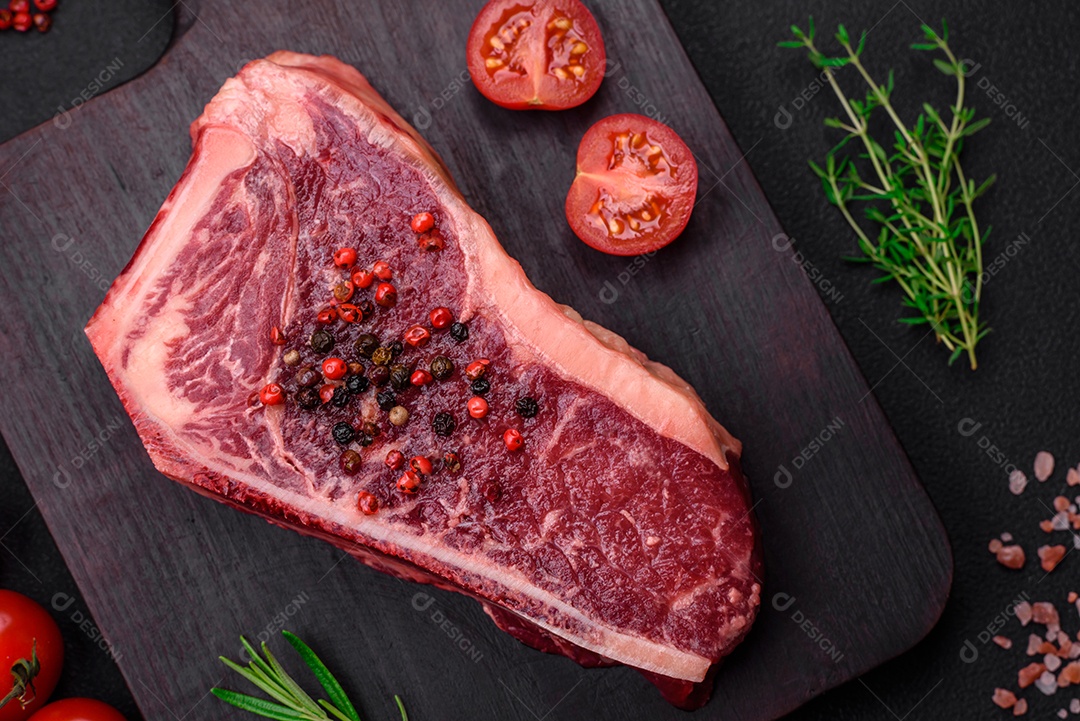 Bife fresco e suculento de Nova Iorque com sal, especiarias e ervas em fundo escuro de concreto