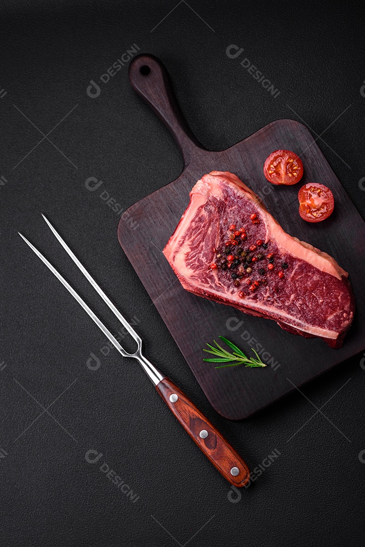 Bife fresco e suculento de Nova Iorque com sal, especiarias e ervas em fundo escuro de concreto