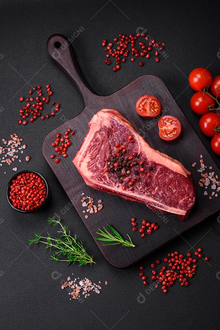 Bife fresco e suculento de Nova Iorque com sal, especiarias e ervas em fundo escuro de concreto