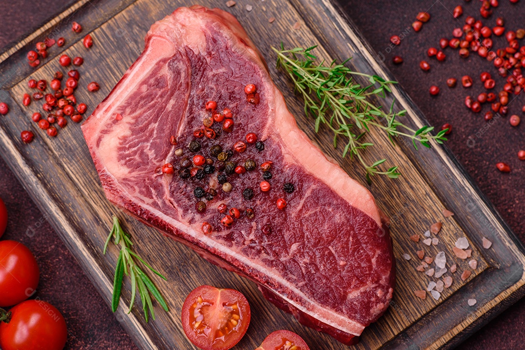 Bife fresco e suculento de Nova Iorque com sal, especiarias e ervas em fundo escuro de concreto