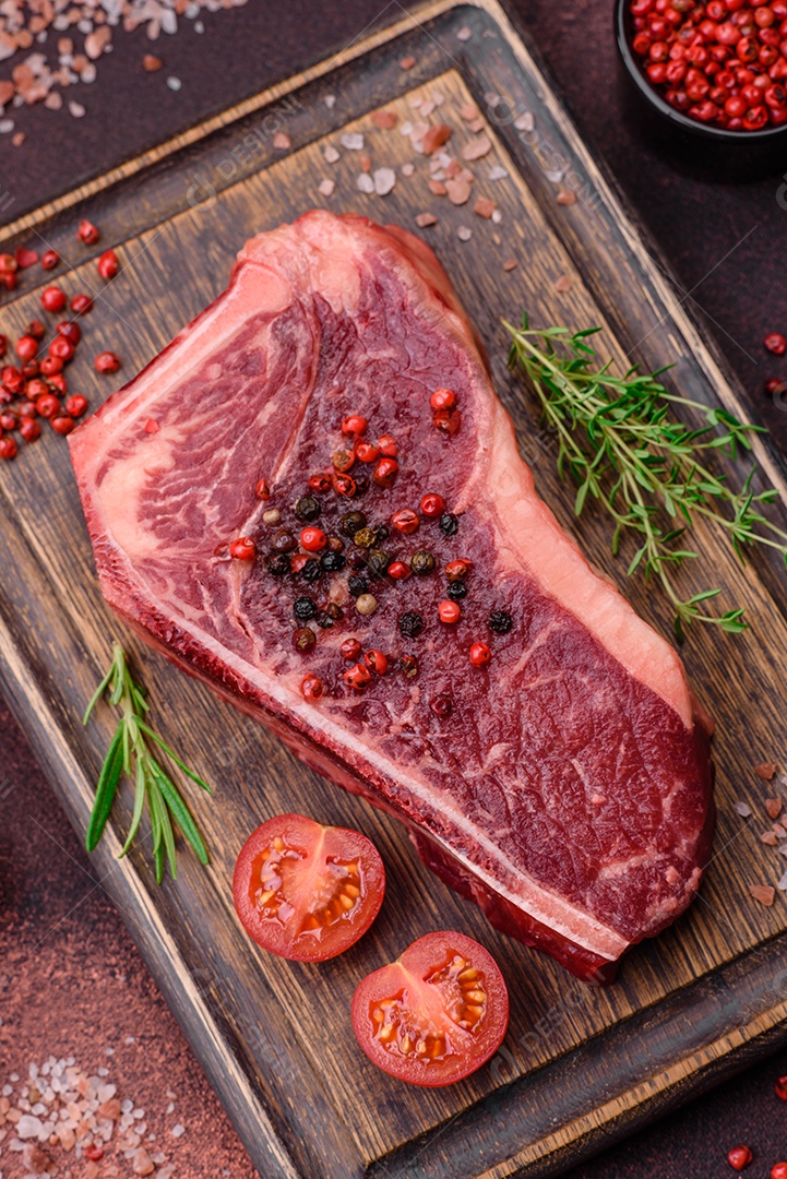 Bife fresco e suculento de Nova Iorque com sal, especiarias e ervas em fundo escuro de concreto