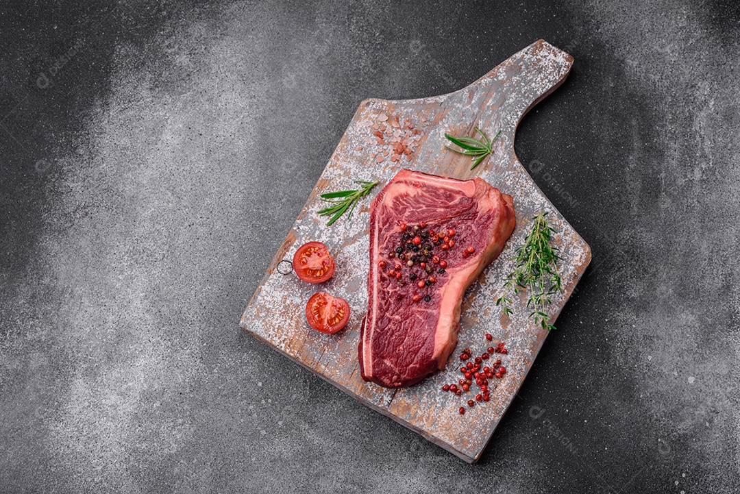 Bife fresco e suculento de Nova Iorque com sal, especiarias e ervas em fundo escuro de concreto