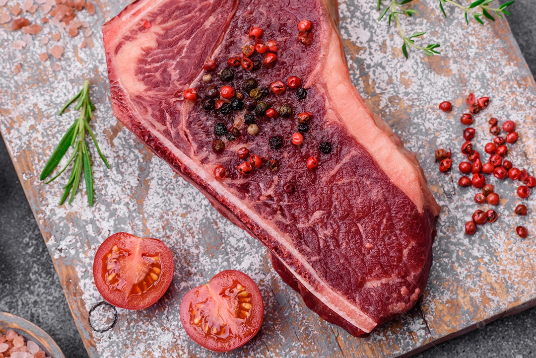 Bife fresco e suculento de Nova Iorque com sal, especiarias e ervas em fundo escuro de concreto