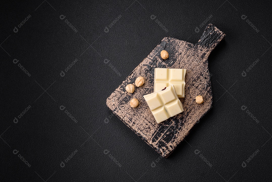 Delicioso chocolate branco doce quebrado em cubos em uma tábua de madeira sobre um fundo escuro de concreto
