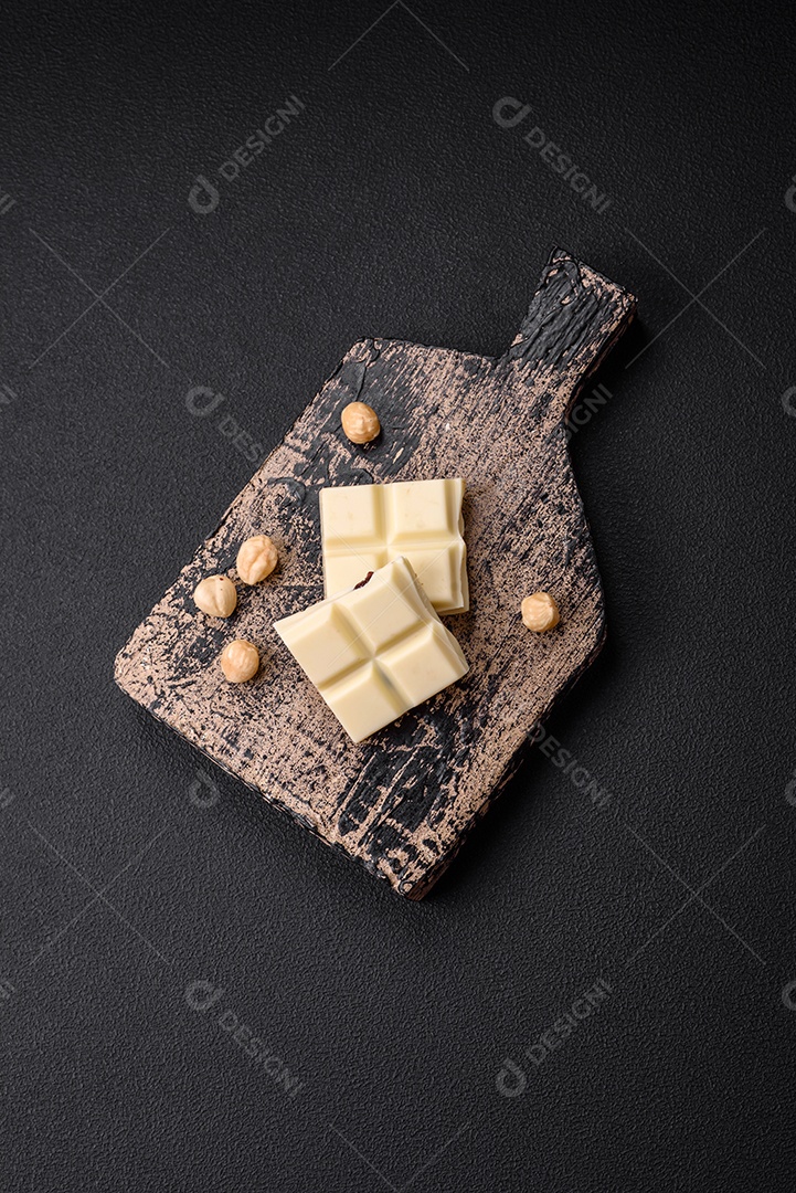 Delicioso chocolate branco doce quebrado em cubos em uma tábua de madeira sobre um fundo escuro de concreto