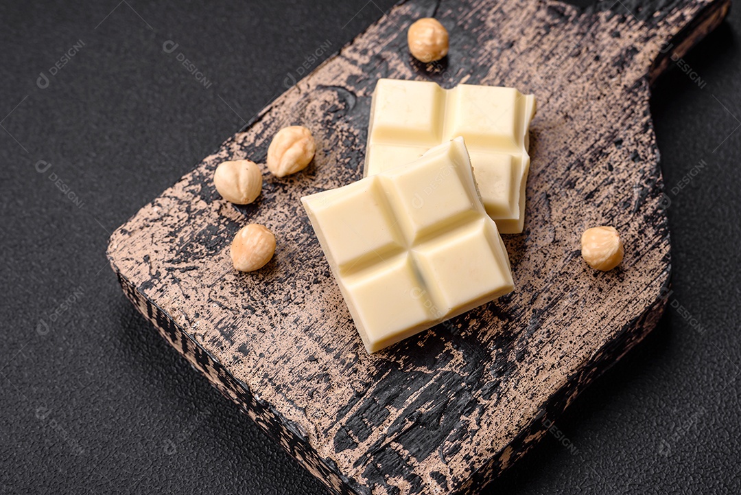 Delicioso chocolate branco doce quebrado em cubos em uma tábua de madeira sobre um fundo escuro de concreto