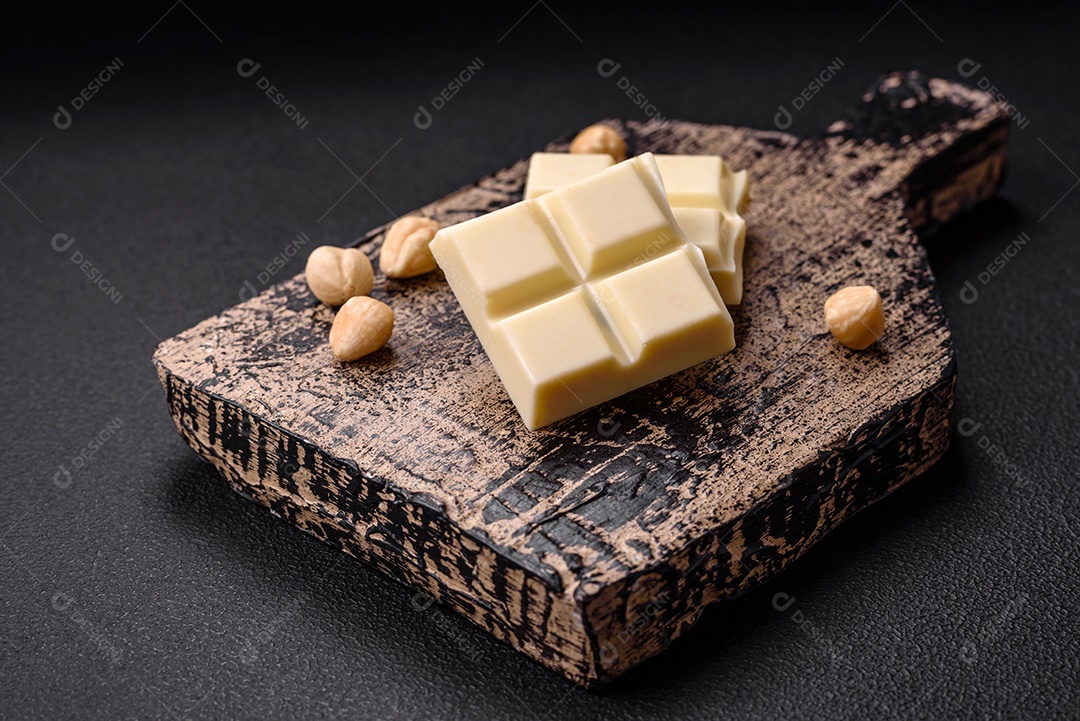 Delicioso chocolate branco doce quebrado em cubos em uma tábua de madeira sobre um fundo escuro de concreto