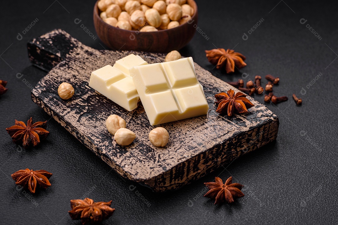 Delicioso chocolate branco doce quebrado em cubos em uma tábua de madeira sobre um fundo escuro de concreto