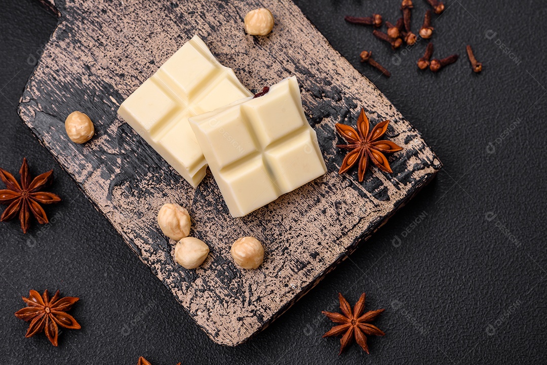 Delicioso chocolate branco doce quebrado em cubos em uma tábua de madeira sobre um fundo escuro de concreto