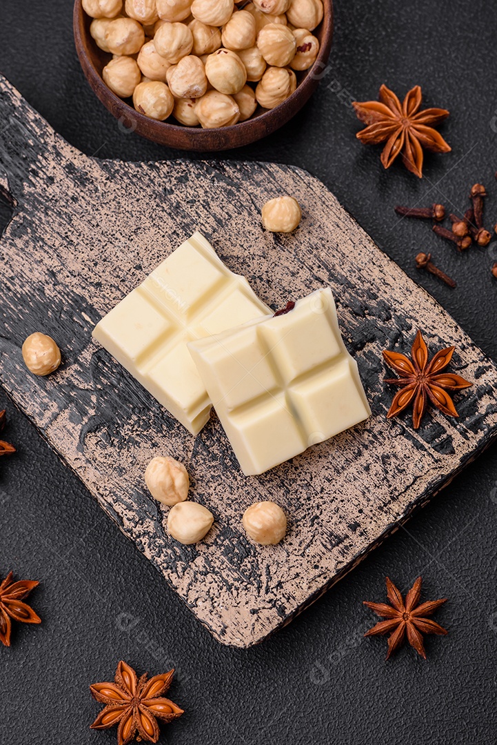 Delicioso chocolate branco doce quebrado em cubos em uma tábua de madeira sobre um fundo escuro de concreto