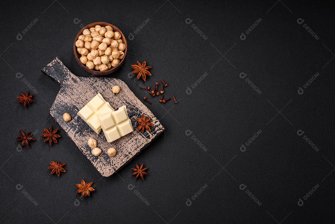 Delicioso chocolate branco doce quebrado em cubos em uma tábua de madeira sobre um fundo escuro de concreto
