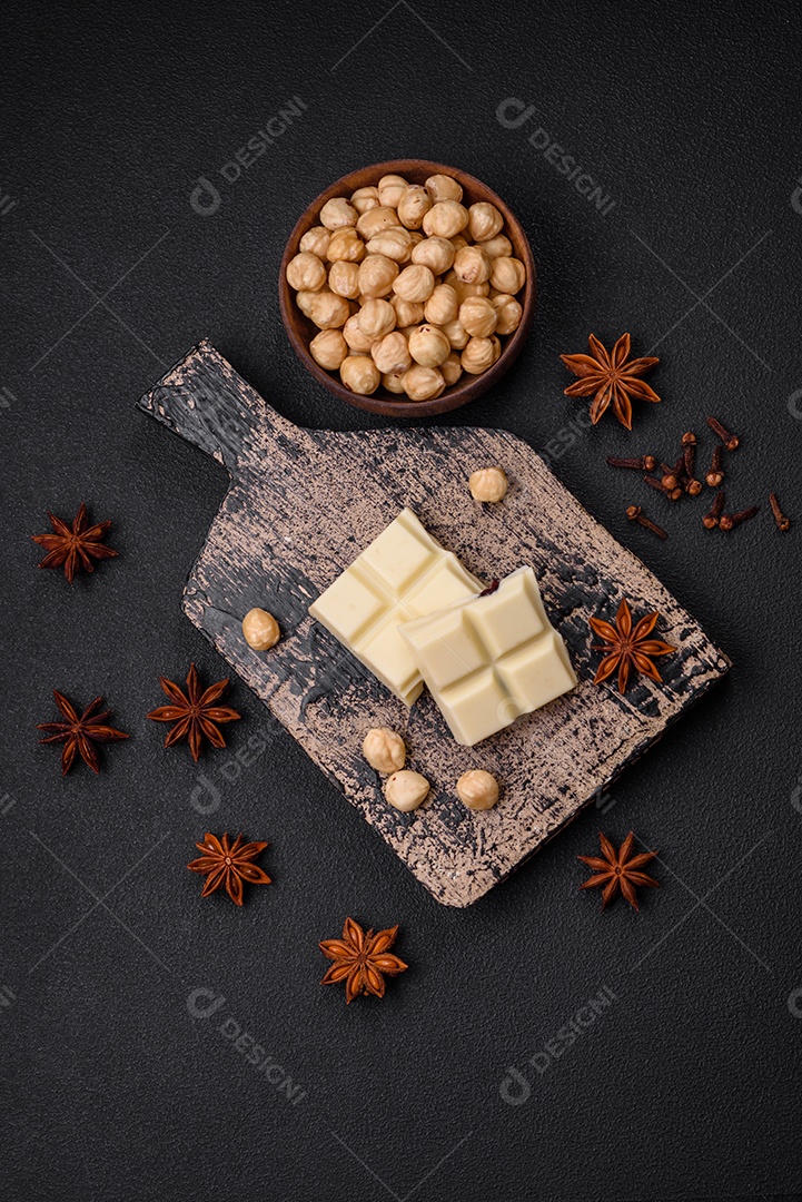 Delicioso chocolate branco doce quebrado em cubos em uma tábua de madeira sobre um fundo escuro de concreto