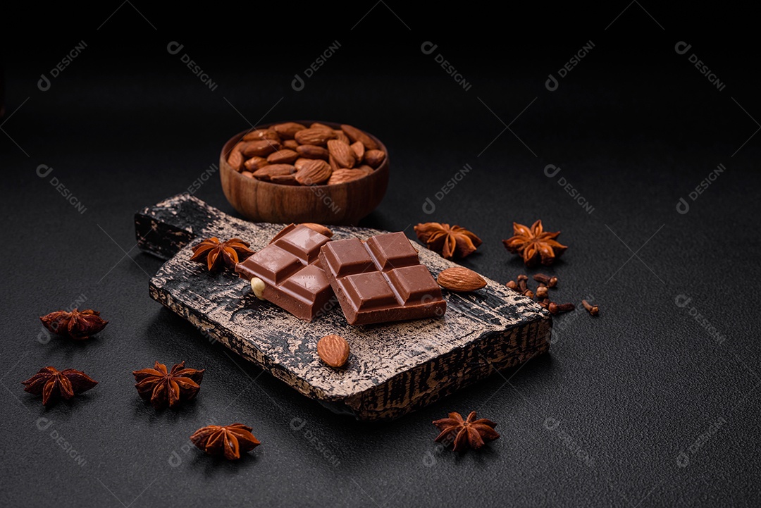 Delicioso chocolate preto doce quebrado em cubos em uma tábua de madeira sobre um fundo escuro de concreto