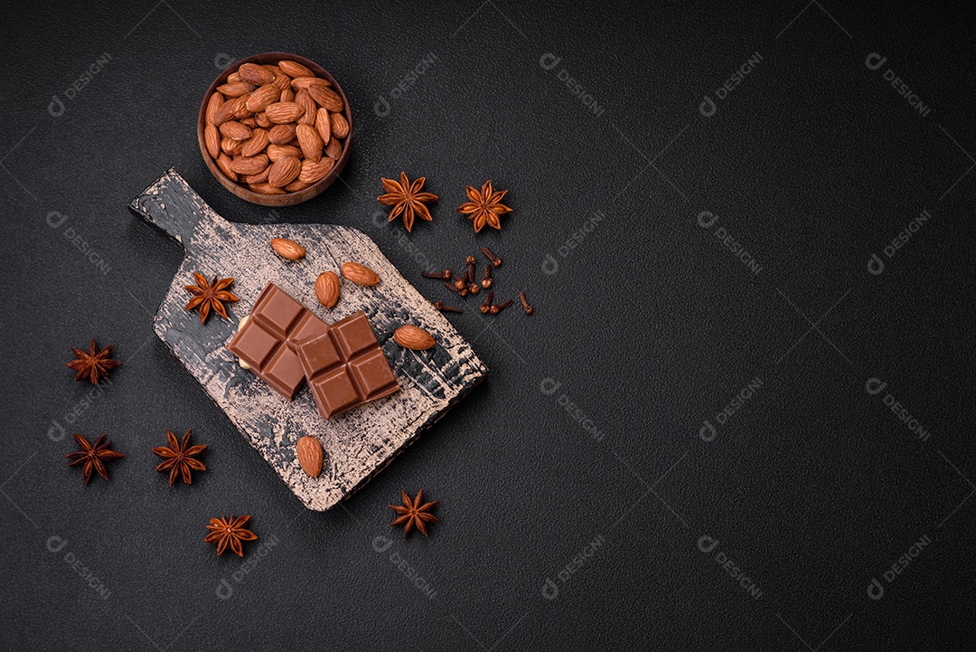 Delicioso chocolate preto doce quebrado em cubos em uma tábua de madeira sobre um fundo escuro de concreto