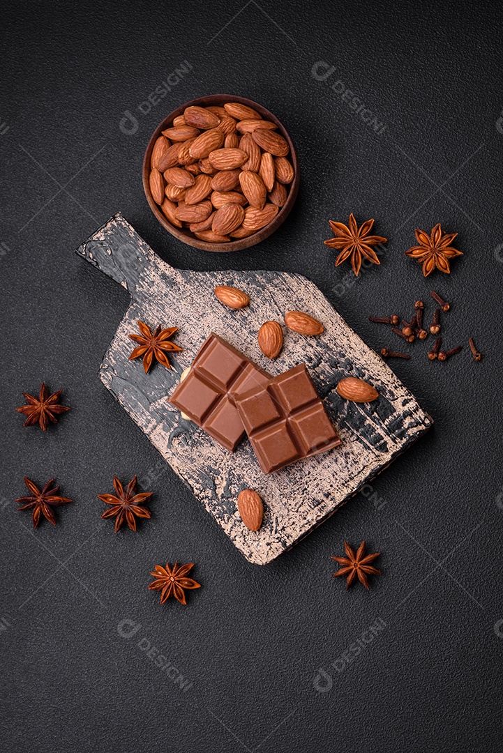 Delicioso chocolate preto doce quebrado em cubos em uma tábua de madeira sobre um fundo escuro de concreto