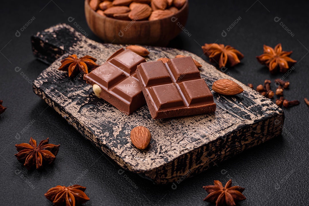 Delicioso chocolate preto doce quebrado em cubos em uma tábua de madeira sobre um fundo escuro de concreto