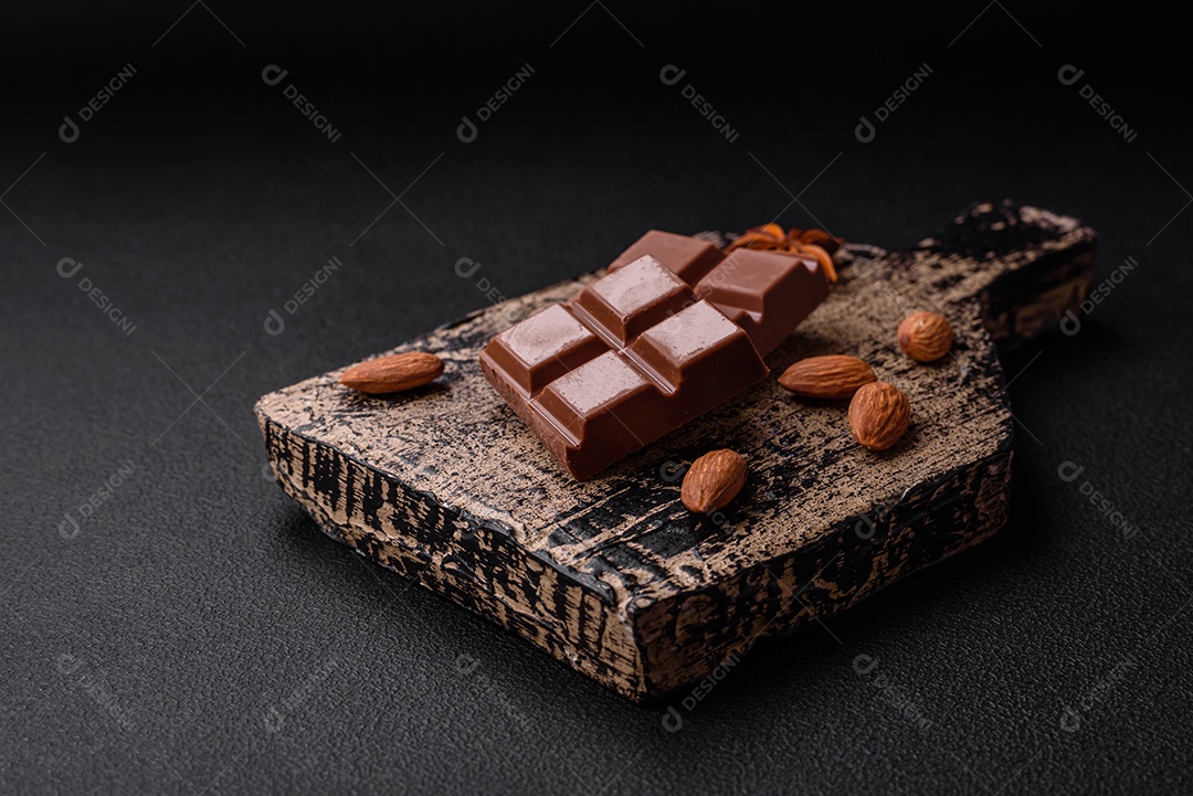 Delicioso chocolate preto doce quebrado em cubos em uma tábua de madeira sobre um fundo escuro de concreto