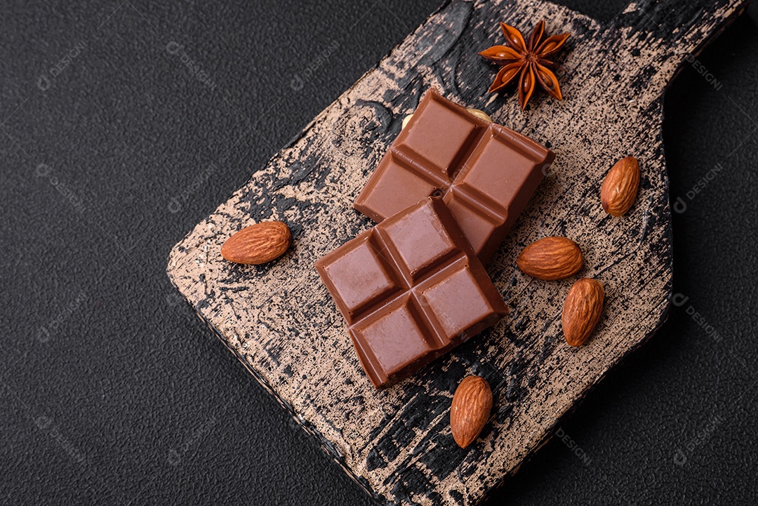 Delicioso chocolate preto doce quebrado em cubos em uma tábua de madeira sobre um fundo escuro de concreto