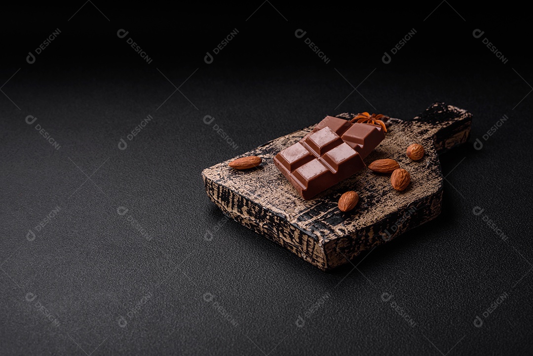 Delicioso chocolate preto doce quebrado em cubos em uma tábua de madeira sobre um fundo escuro de concreto