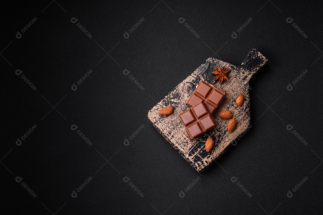 Delicioso chocolate preto doce quebrado em cubos em uma tábua de madeira sobre um fundo escuro de concreto