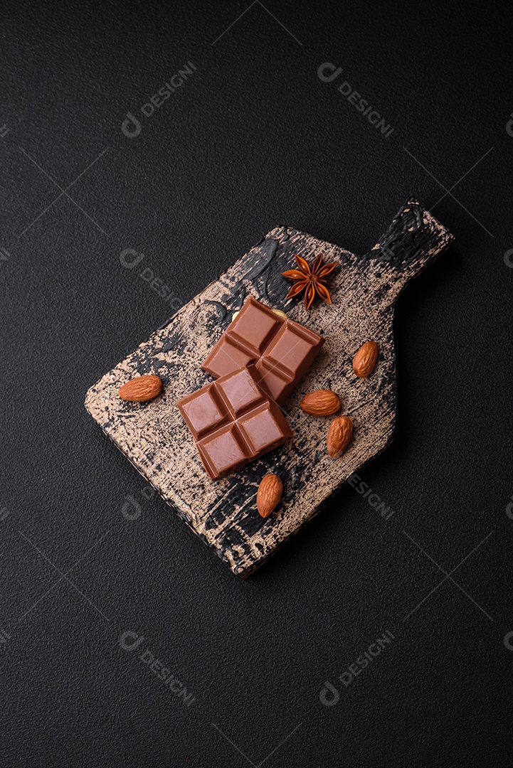 Delicioso chocolate preto doce quebrado em cubos em uma tábua de madeira sobre um fundo escuro de concreto