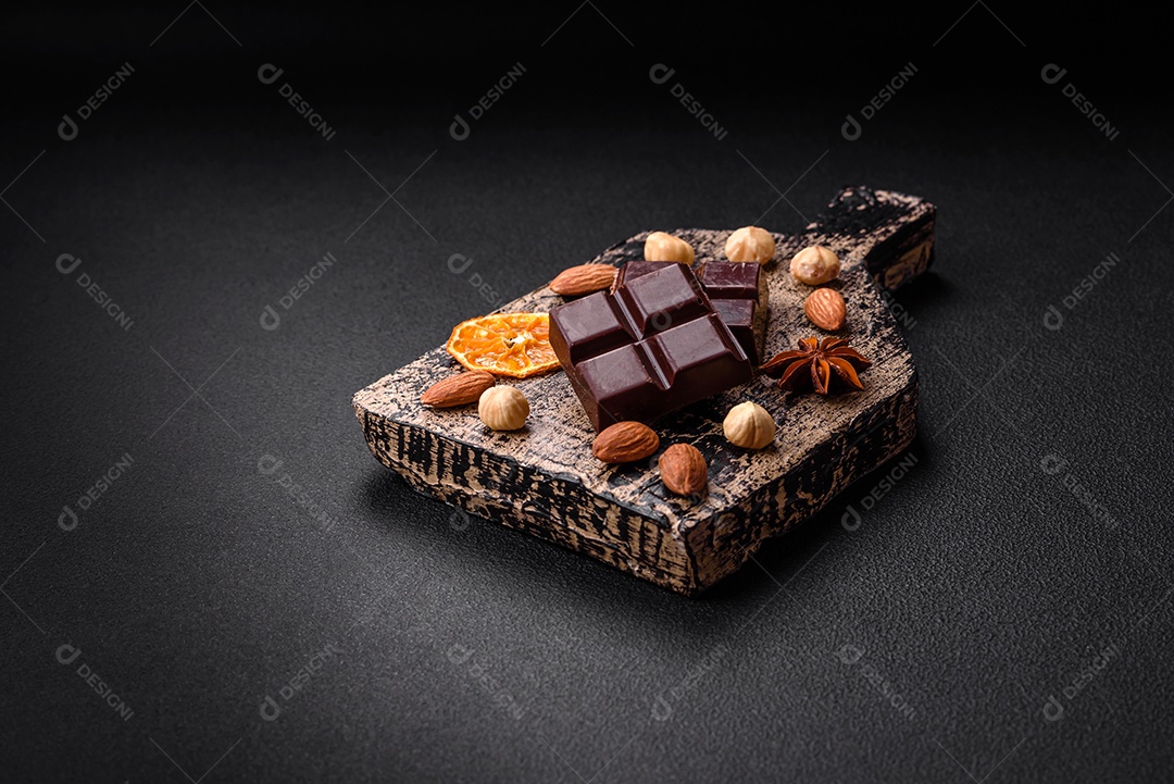 Delicioso chocolate preto doce quebrado em cubos em uma tábua de madeira sobre um fundo escuro de concreto