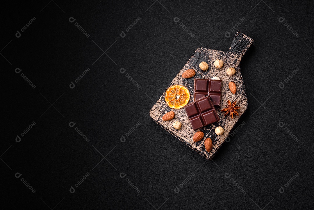 Delicioso chocolate preto doce quebrado em cubos em uma tábua de madeira sobre um fundo escuro de concreto