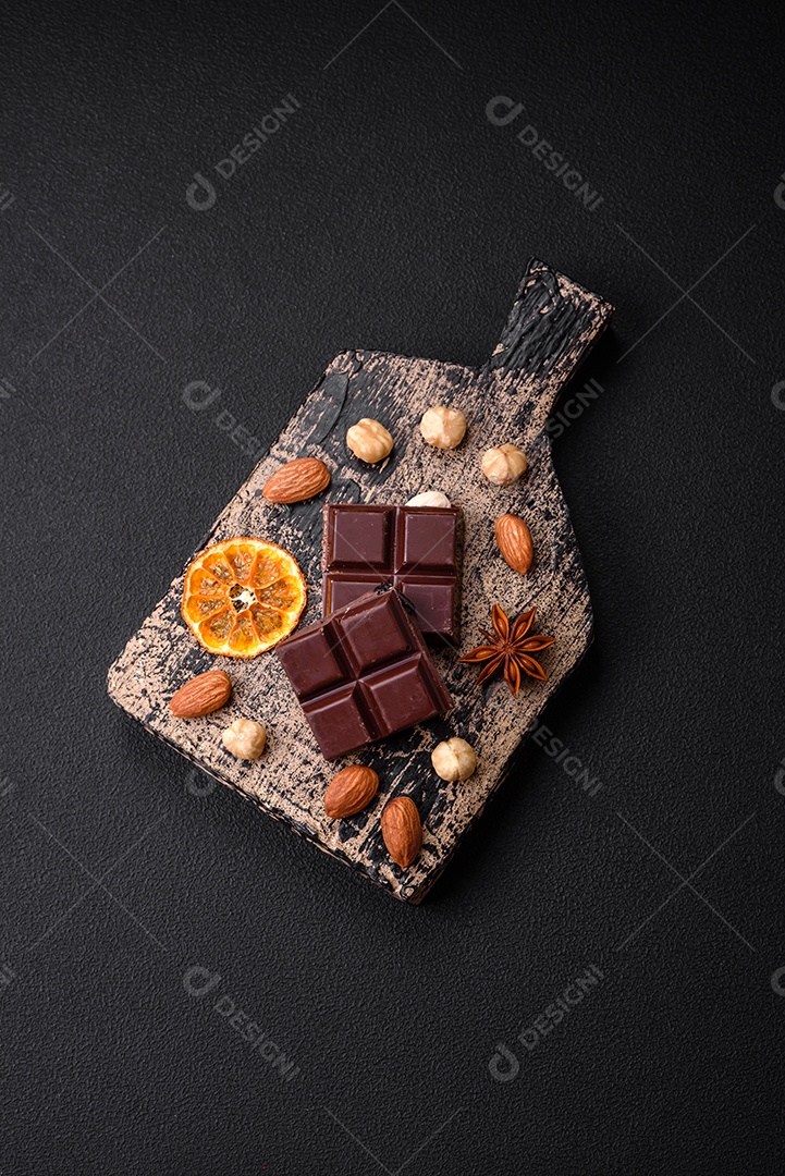 Delicioso chocolate preto doce quebrado em cubos em uma tábua de madeira sobre um fundo escuro de concreto