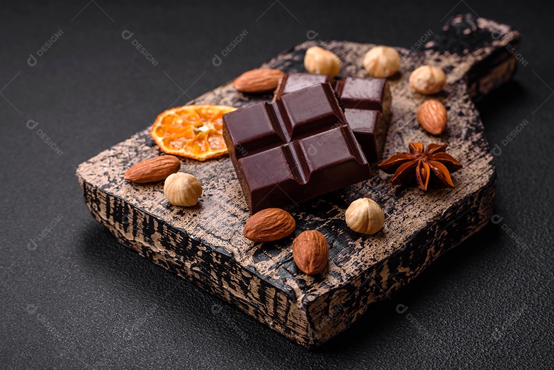 Delicioso chocolate preto doce quebrado em cubos em uma tábua de madeira sobre um fundo escuro de concreto